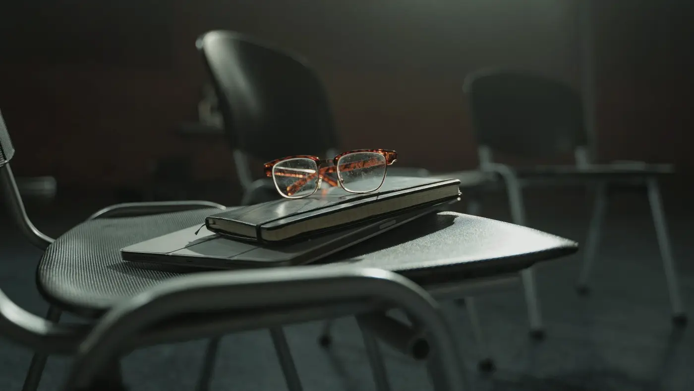 Des lunettes posées sur un carnet, sur une chaise de salle de réunion vide : apprendre à juger l'IA se prépare avant de s'en servir.