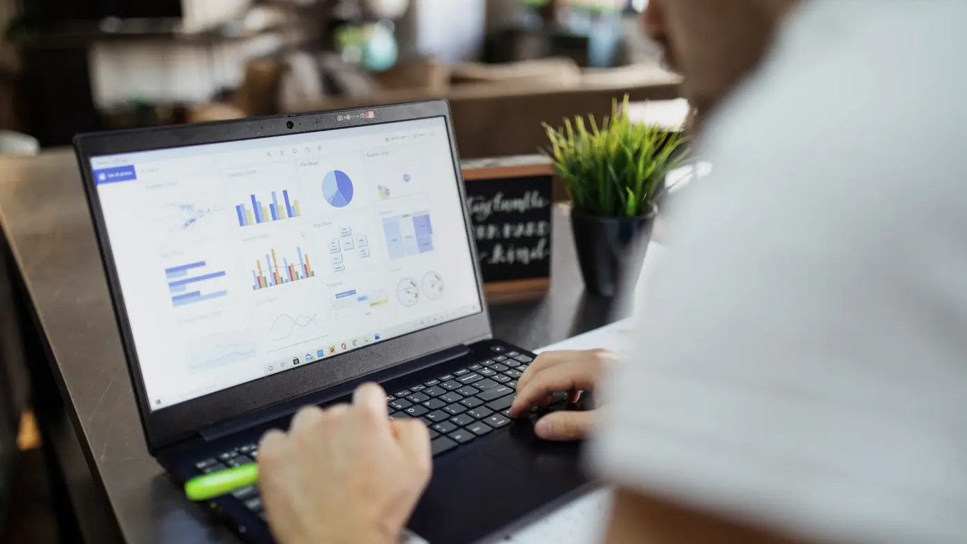 Une personne travaille sur un ordinateur portable affichant des graphiques de tableur : rien ne distingue une valeur produite par une IA d'un résultat calculé.