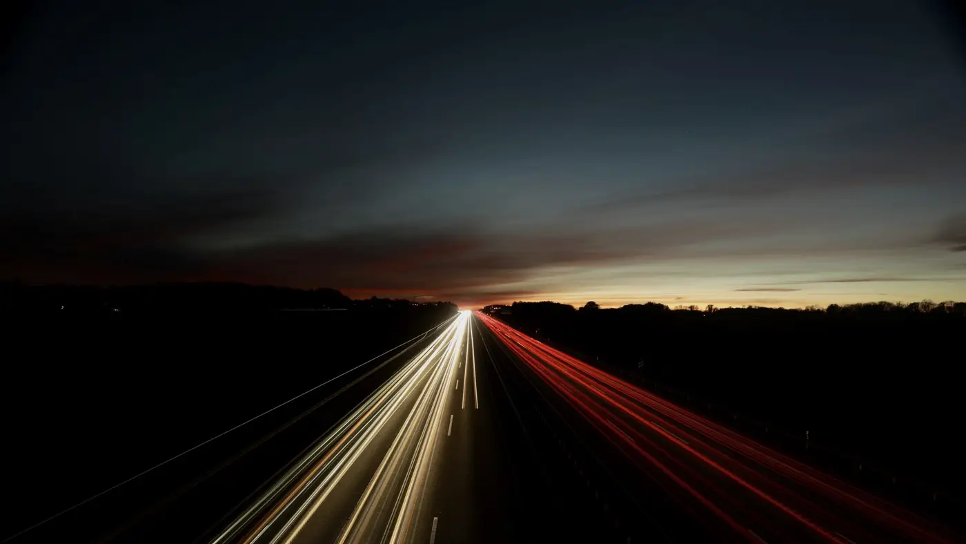 Des traînées de phares sur une autoroute au crépuscule : les trajets successifs d'une flotte suffisent à dessiner ses habitudes.