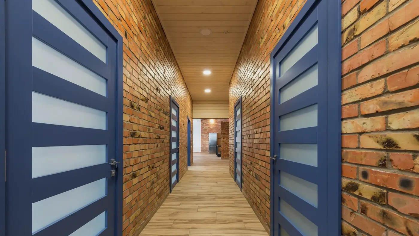 Un couloir d'immeuble aux portes fermées : une commande de travaux associe un logement, ses occupants et la date du passage d'un intervenant.