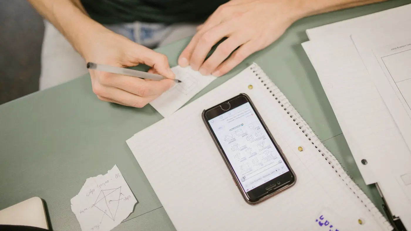 Un étudiant travaille à son bureau, téléphone posé sur son cahier : avec un IBAN, un nom et une date de naissance, un escroc peut se faire passer pour un conseiller bancaire.