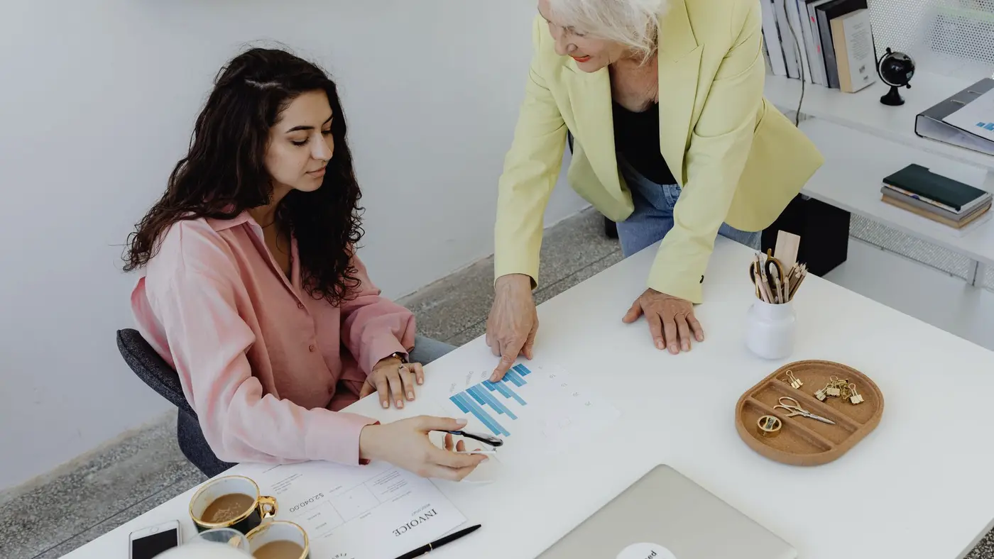 Une responsable commente un graphique avec une jeune collègue à son bureau : selon PwC, les postes exposés à l'IA demandent plus tôt des compétences de jugement.